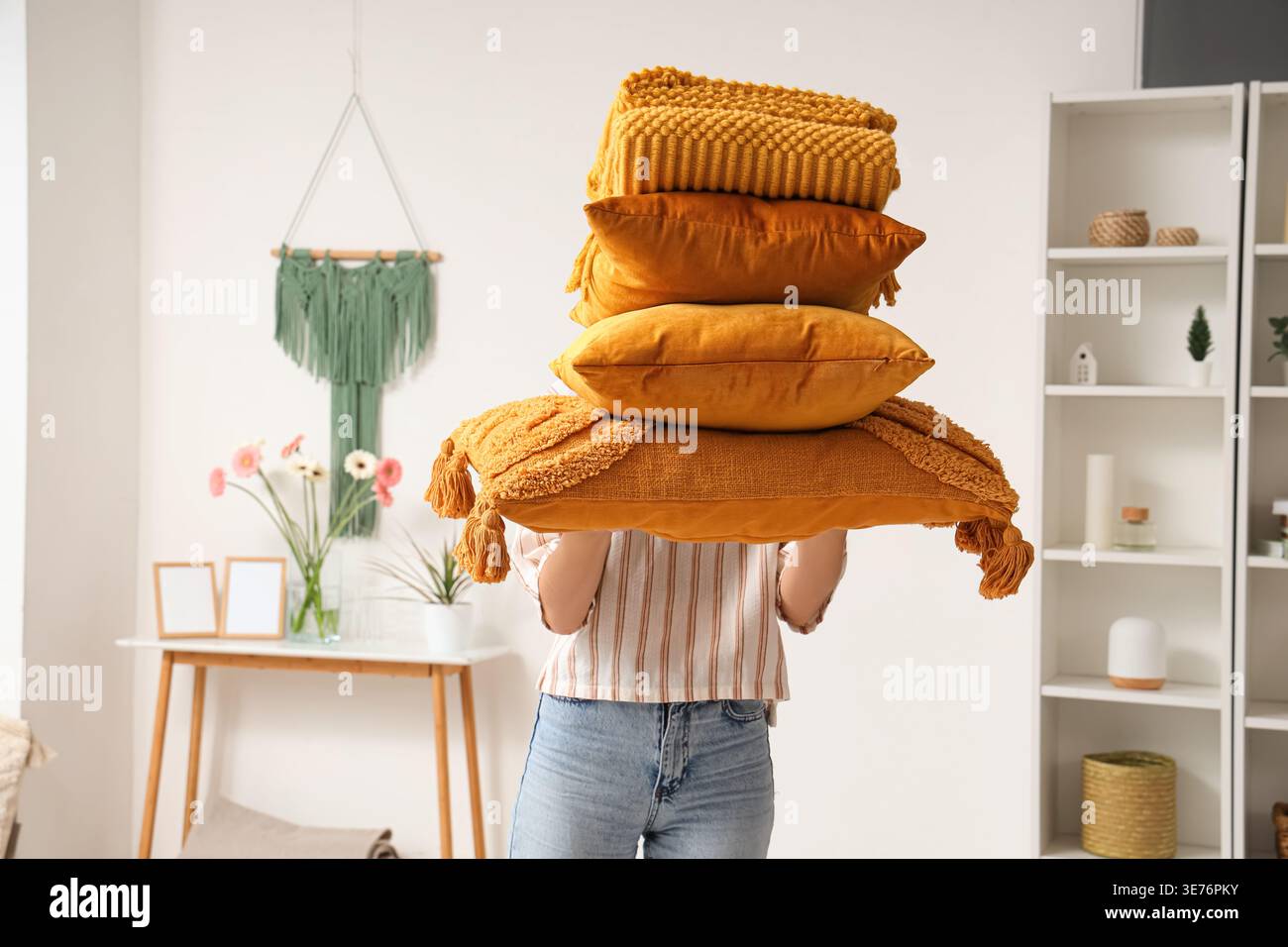Woman holding stack of pillows with folded warm plaid in room Stock Photo
