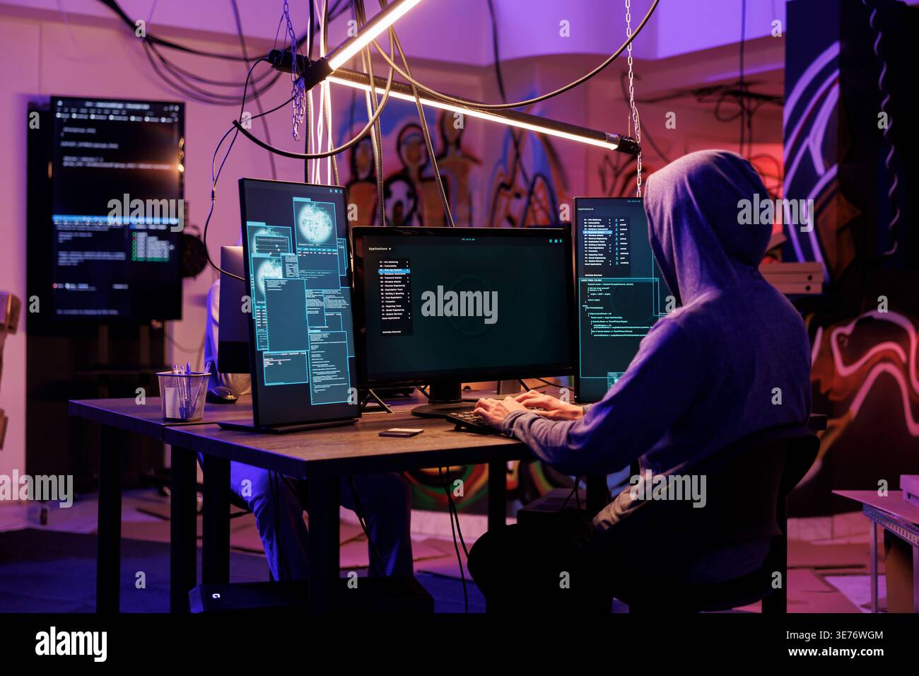 Hacker in hood using spyware to steal information from server while coding on computer with multiple screens. Man programming illegal malicious software in hideout place Stock Photo