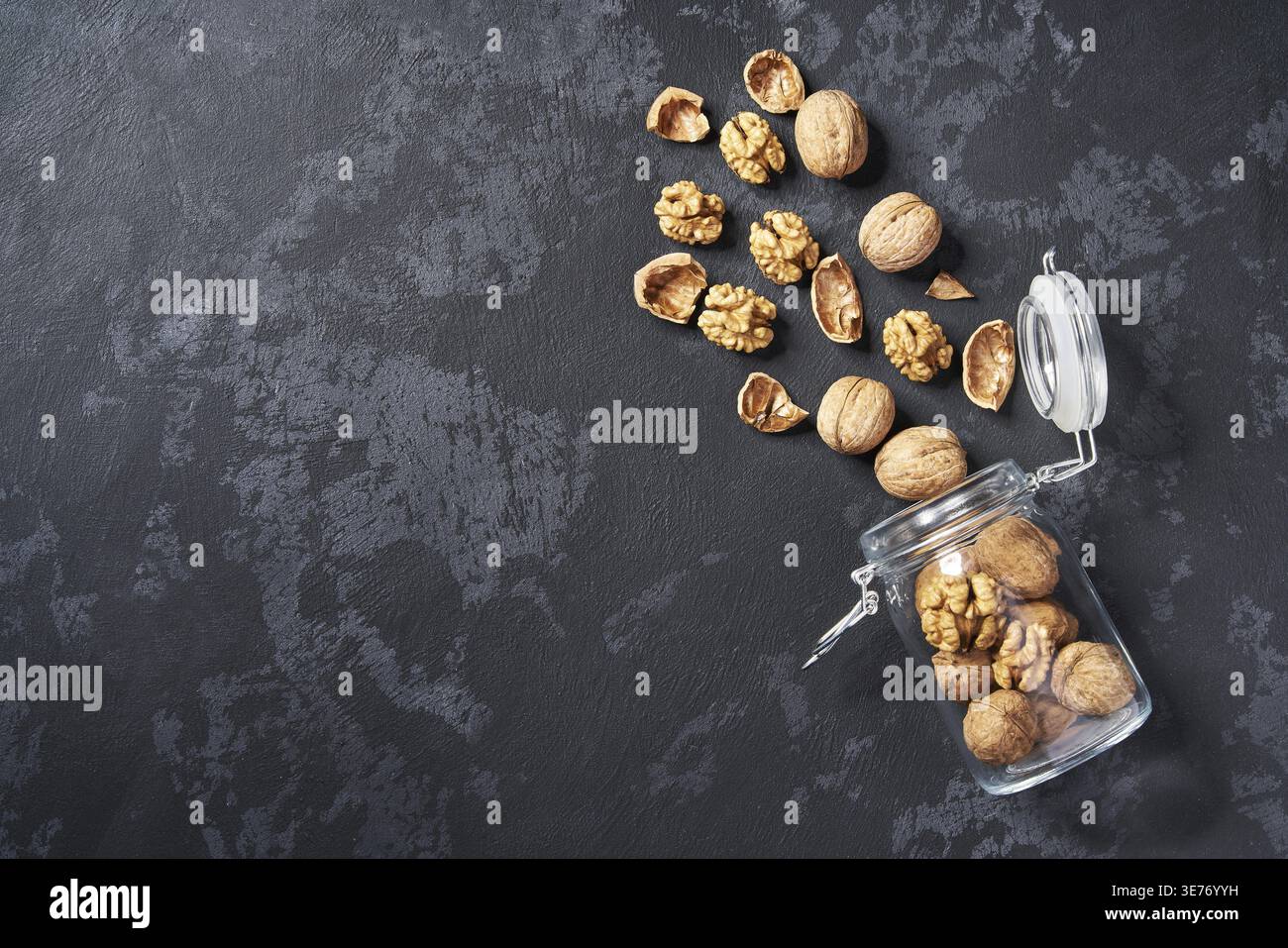 Peeled and unpeeled walnuts in an open glass container on a black table, with copy space. View from above Stock Photo