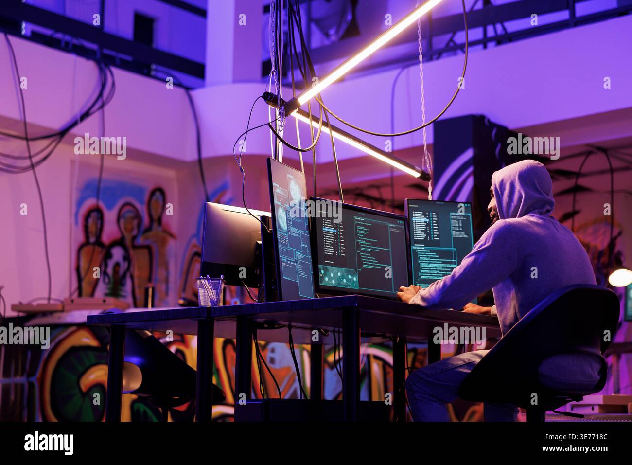 Hacker developing internet virus for data breaching and hacking server in dark warehouse. Man in hood running malware code for password cracking on computer screen in room at night Stock Photo