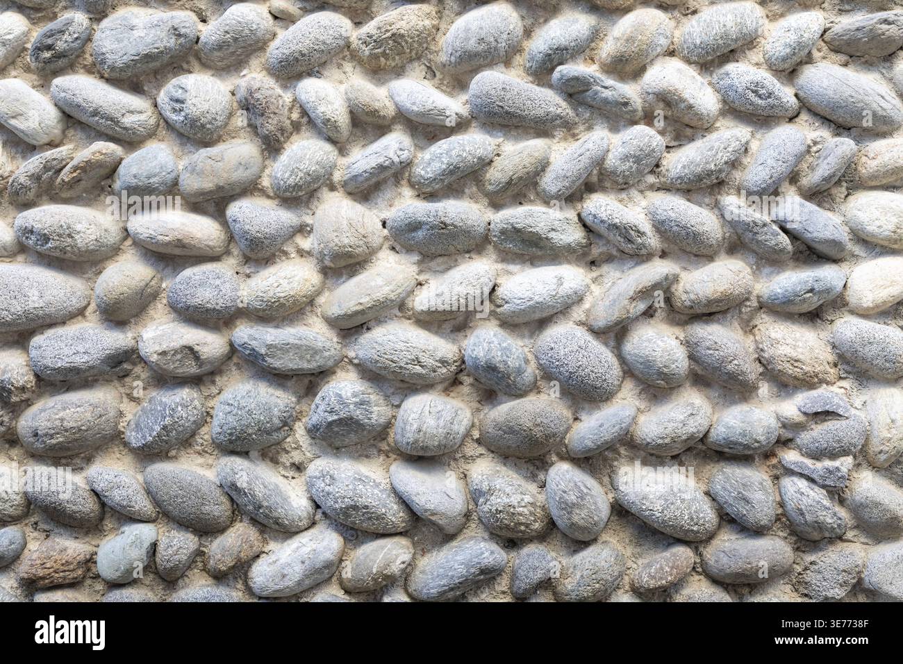 Close-up of a pebble stone wall surface made of smooth rounded rocks. Natural pattern and neutral tones create a calm, balanced, and timeless architec Stock Photo