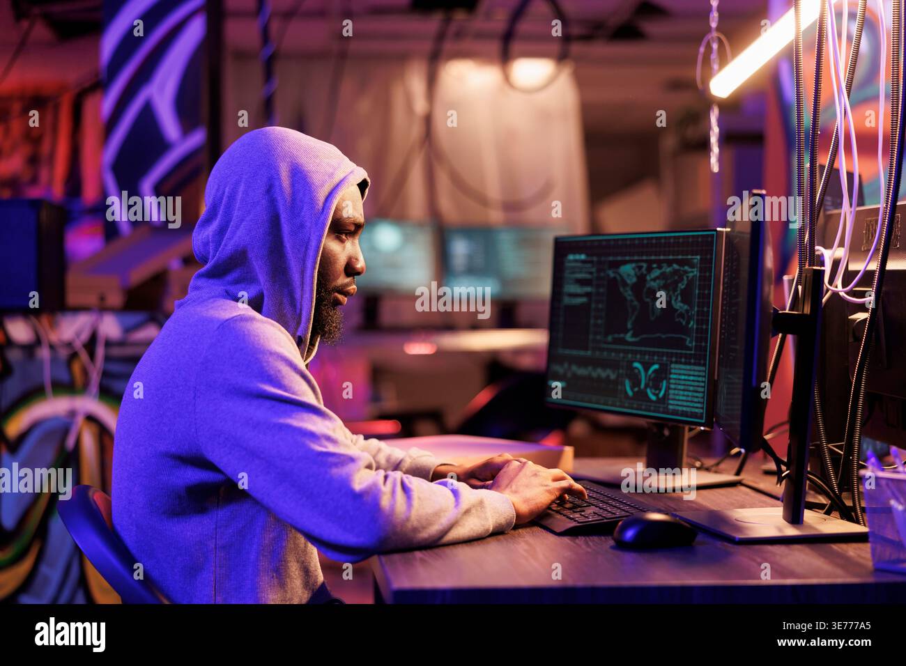 African american hacker coding spyware in abandoned warehouse. Man in hood using computer for breaching data, cracking password and getting access to server database at night Stock Photo