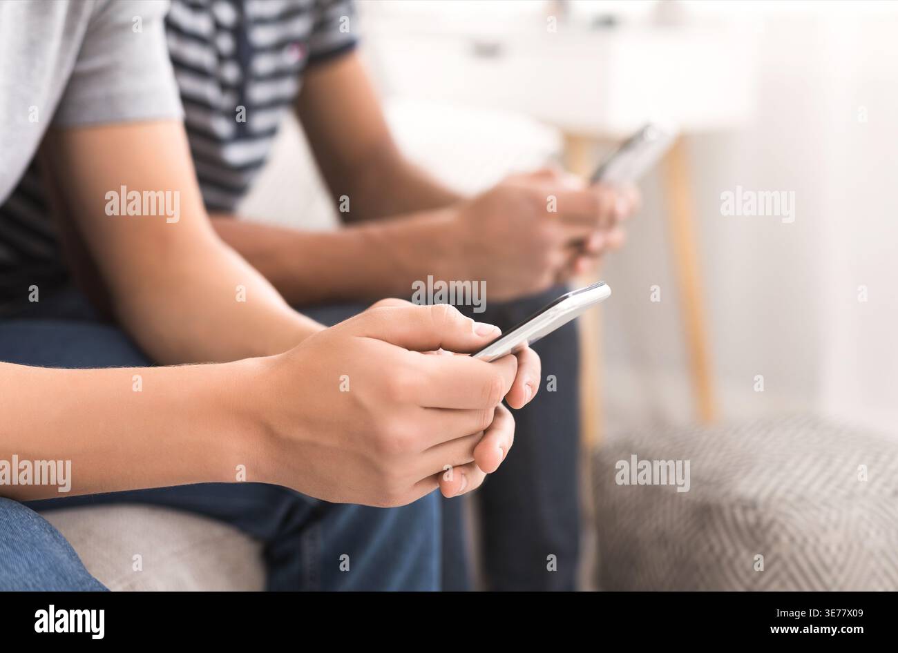 Two friends using smartphones while sitting on sofa Stock Photo