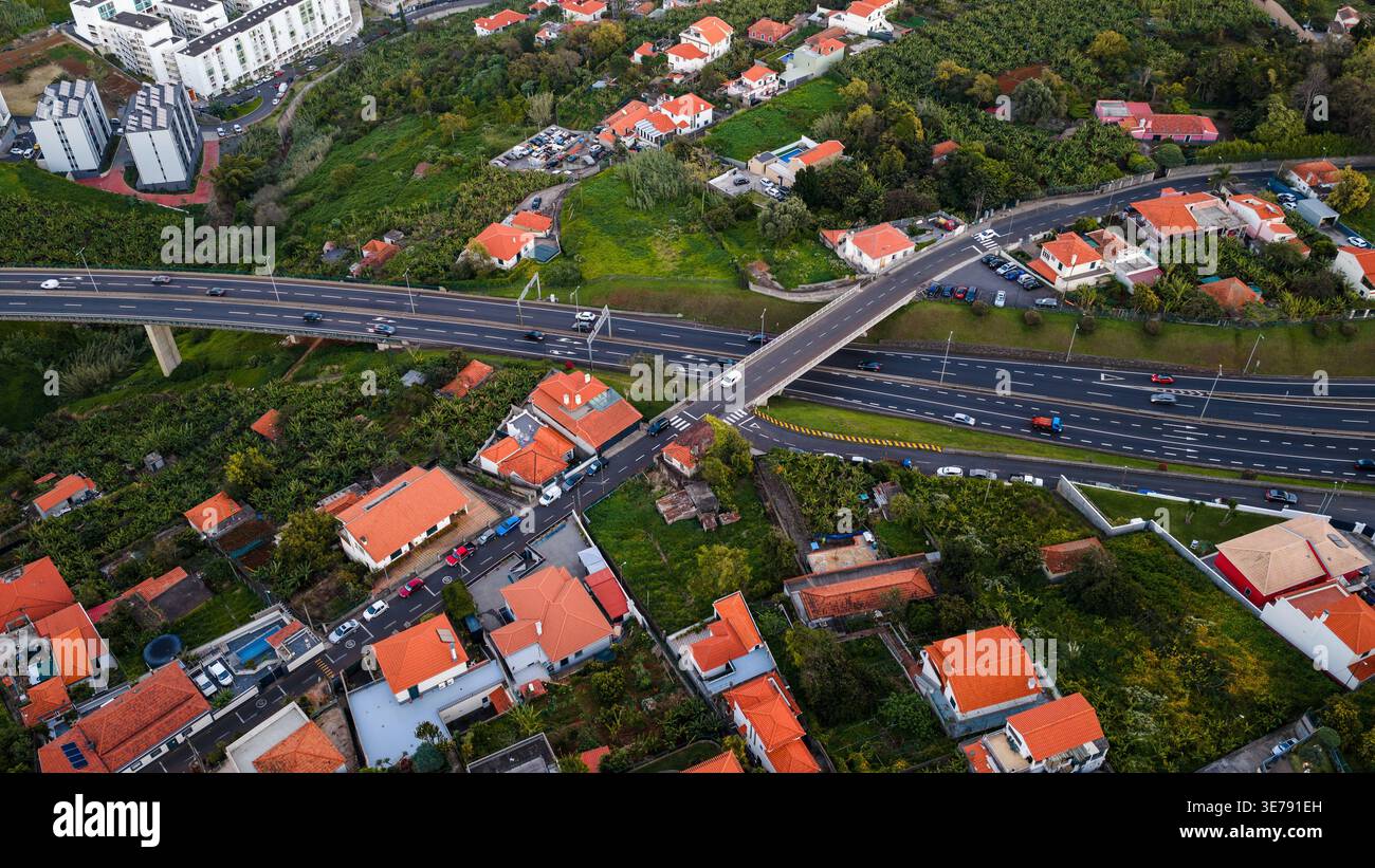 Aerial view of a sweeping overpass and multilane traffic on Madeira, Portugal, with terraced gardens, banana plantations, and white houses with orange Stock Photo