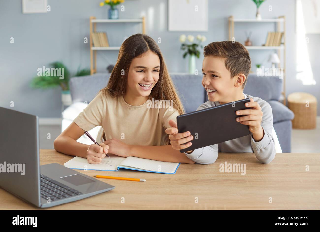 Two children are happily doing their homework and having fun using modern gadgets. Stock Photo