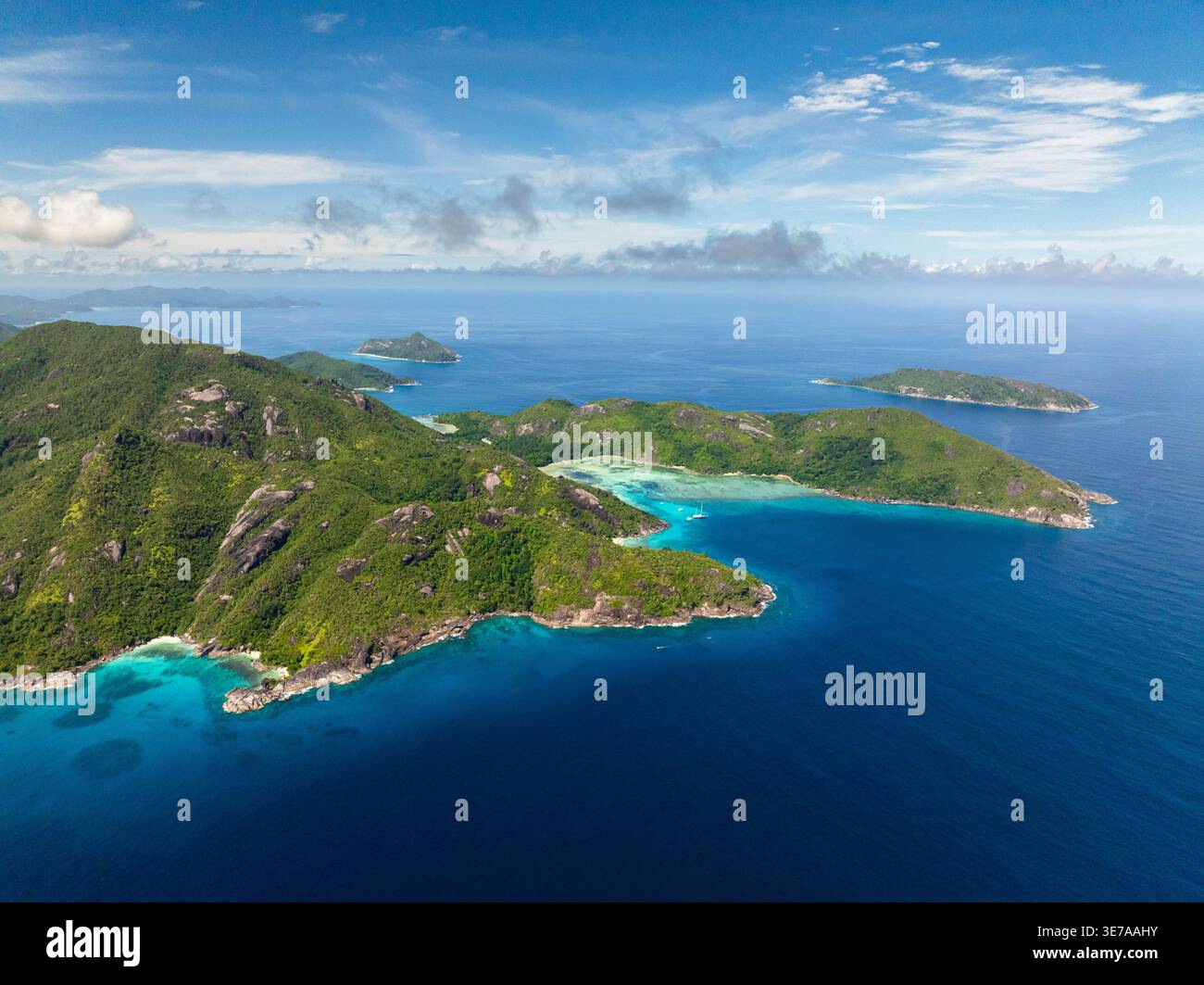 Vast green mountains and turquoise bay stretch out under a bright blue sky with clear waters. Seychelles, Mahe. Stock Photo