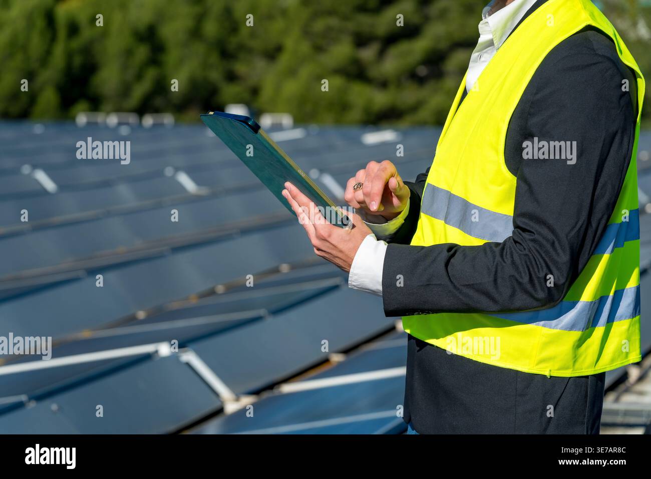 Cropped image of Hispanic male engineer in safety vest and suit jacket holding clipboard and pen while inspecting and recording data from large out... Stock Photo