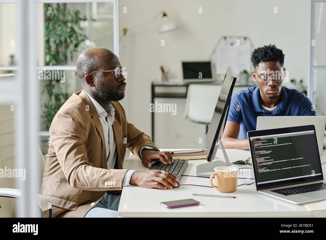 Serious Black male programmers sitting at desk developing new software on computers working together in office Stock Photo