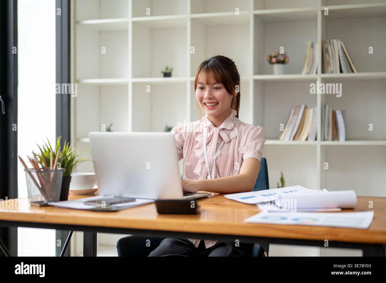 Smiling Asian woman working on laptop sutting at table in office Stock Photo