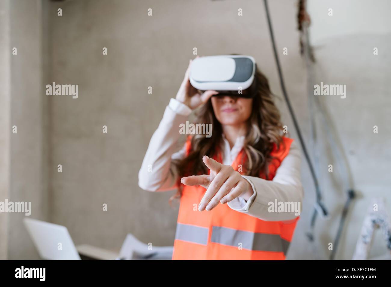 Hispanic female architect using VR headset pointing forward standing in construction site during daytime Stock Photo