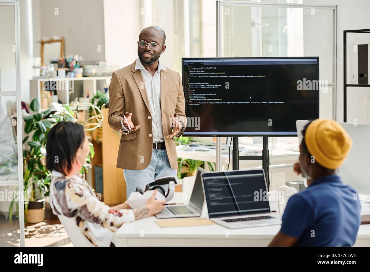 Black male programmer wearing eyeglasses discussing codes while standing in front of colleagues in office Stock Photo