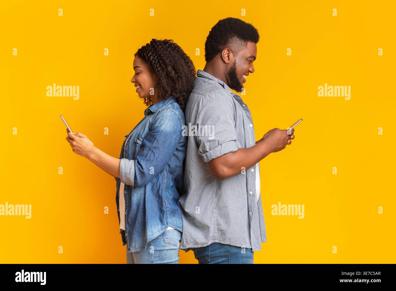 Black couple standing back to back while using their smartphone against yellow background Stock Photo