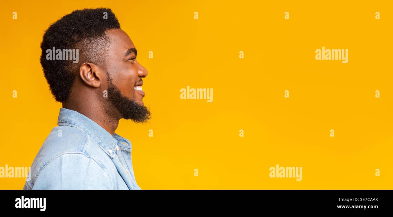Black man with beard standing sideways against yellow background in studio Stock Photo