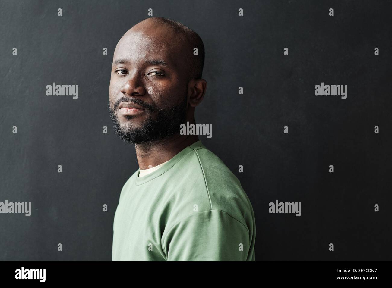 Black man with beard standing sideways against black wall at home Stock Photo