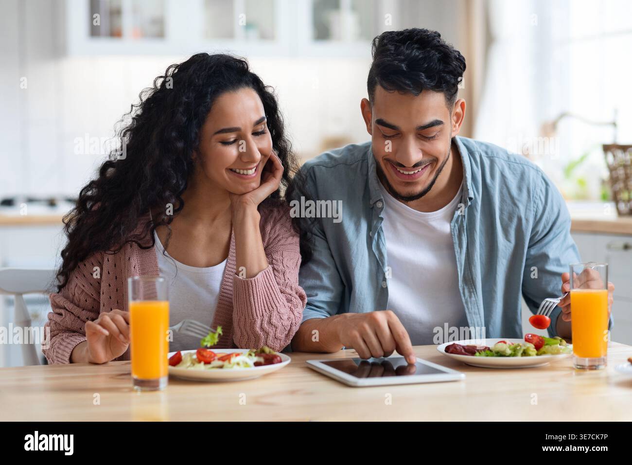 Smiling Middle Eastern couple having breakfast using tablet while sitting at table at home Stock Photo