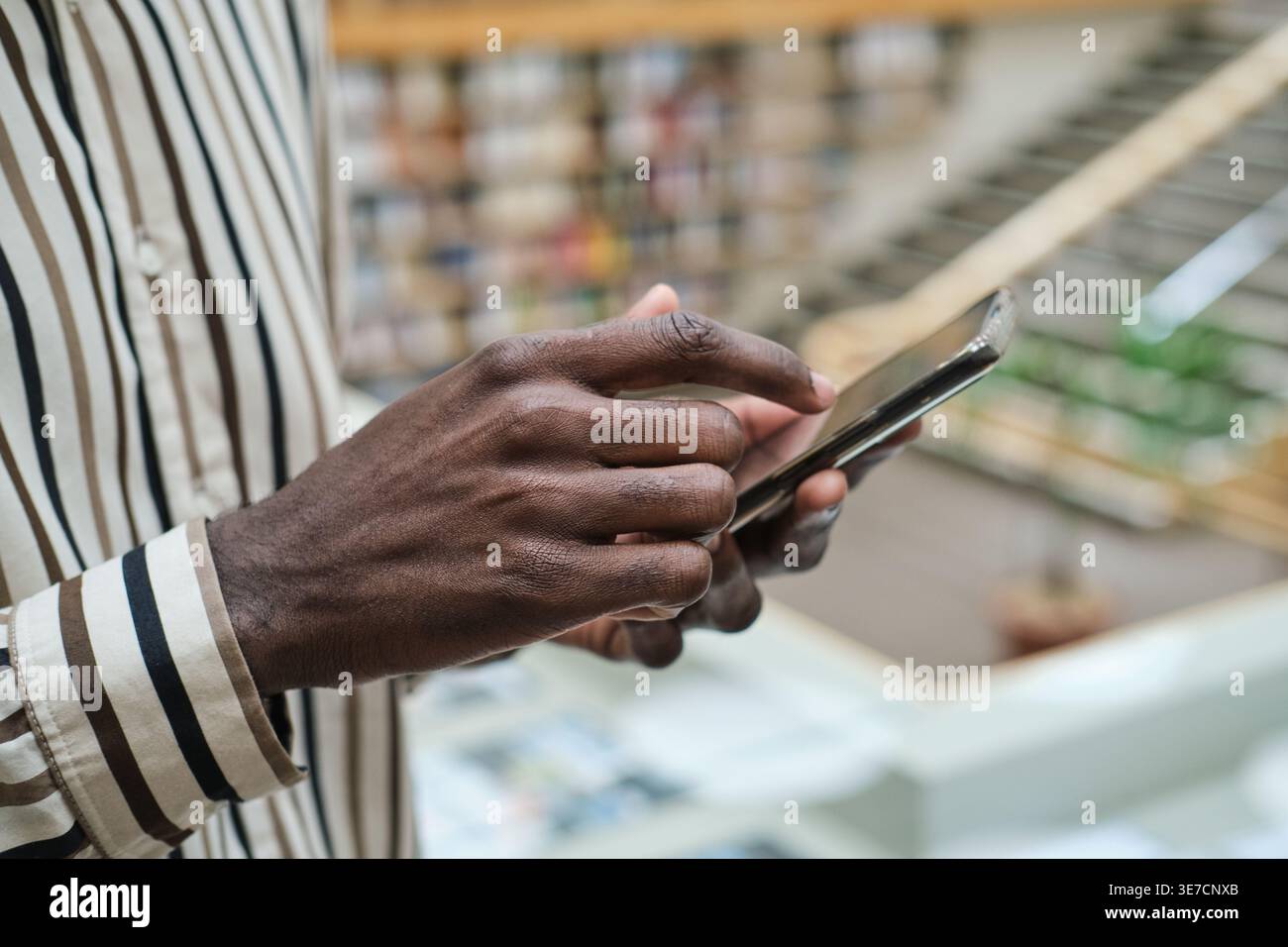 Black man wearing stripe long sleeves using smartphone while standing in library Stock Photo