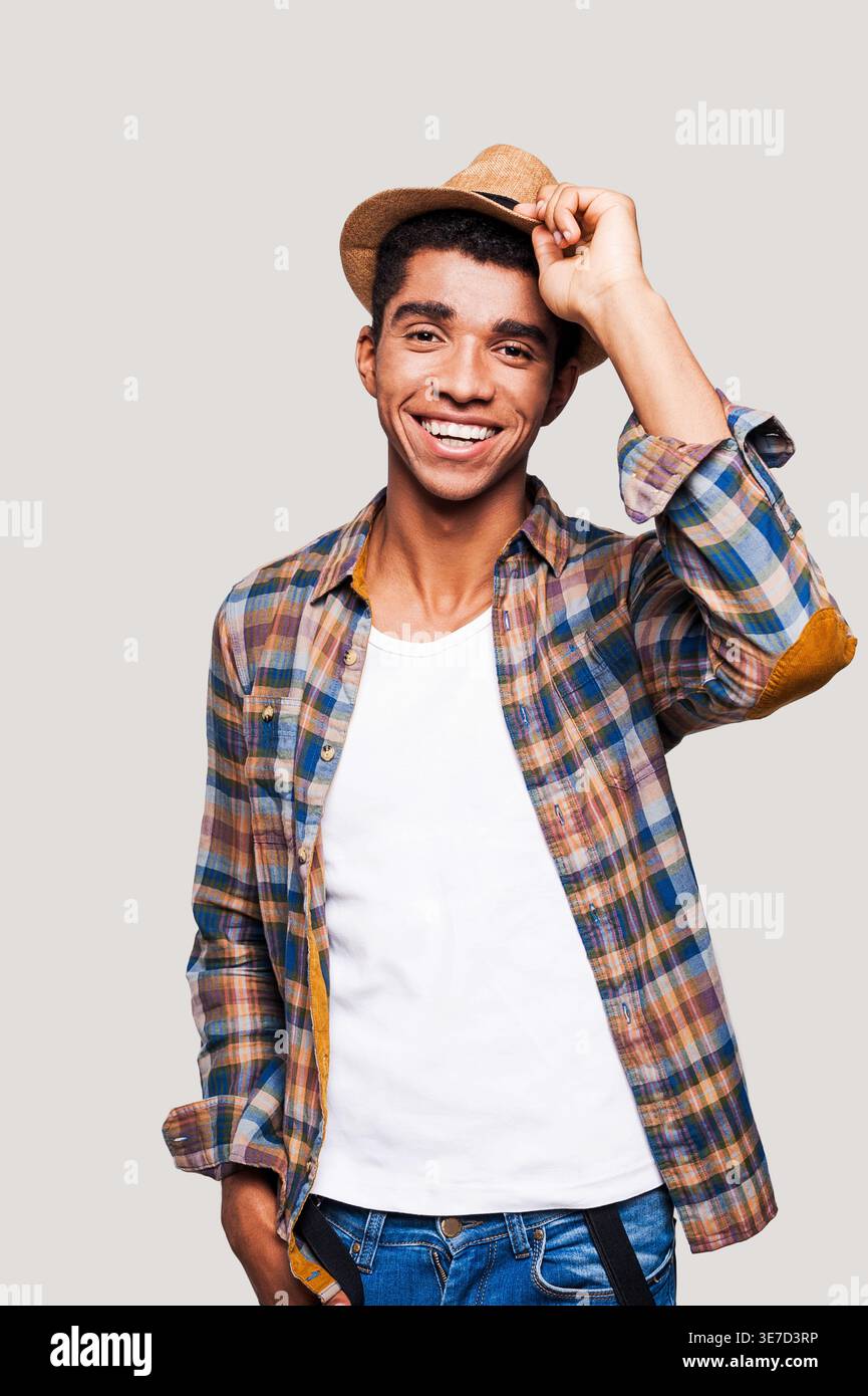 Black man tipping straw hat while standing against light gray background Stock Photo