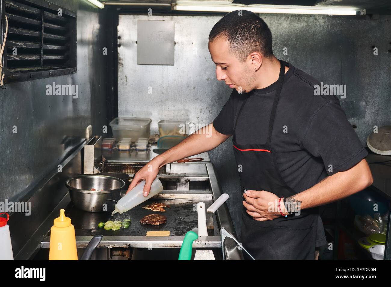 Side view of ethnic male cook standing at stove and pouring oil on ...