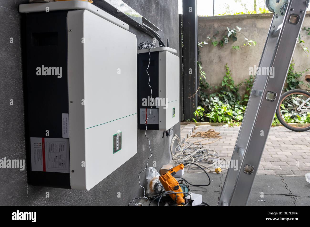 Complete solar energy system installed on a wall, including batteries, inverter units and PV combiner box with visible wiring and tools. installation Stock Photo