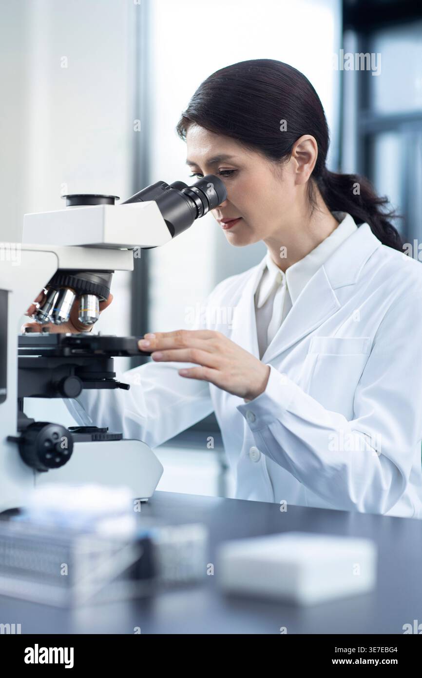 Chinese female scientist looking through microscope while working in laboratory Stock Photo