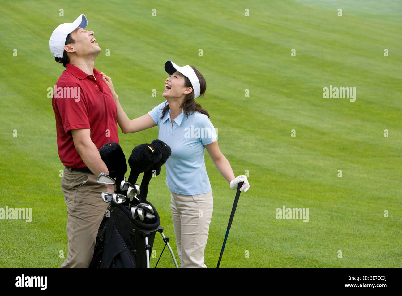 Smiling Chinese couple playing golf while standing on golf course Stock Photo