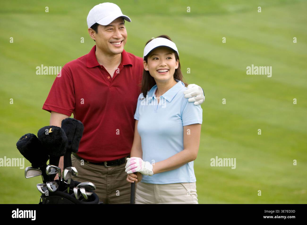 Smiling Chinese couple playing golf while standing on golf course Stock Photo