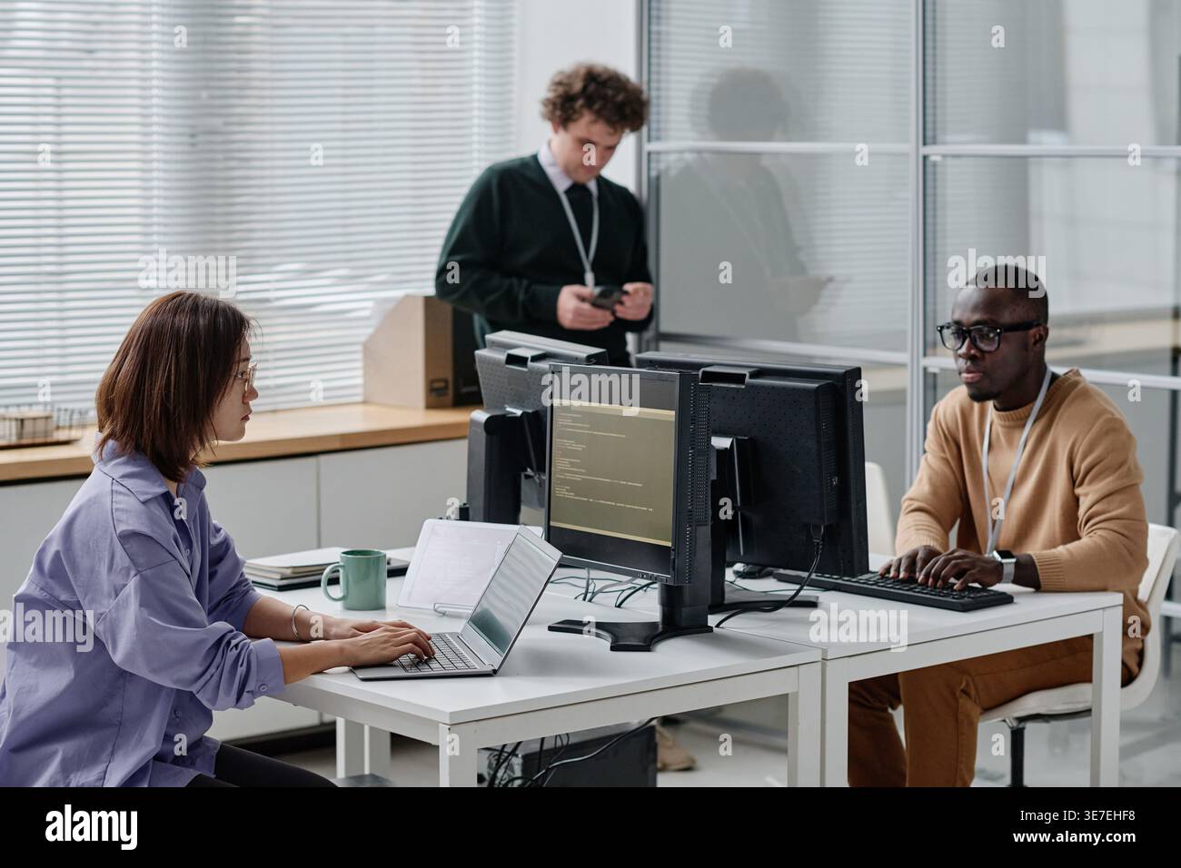 Group of diverse developers sitting at desk writing codes for new computer program in IT office Stock Photo