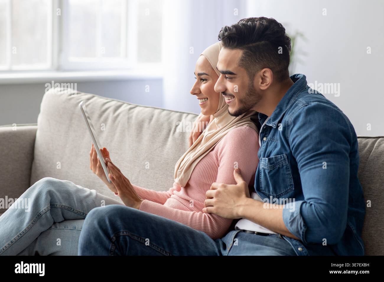 Smiling Middle Eastern couple using tablet while sitting on sofa at home Stock Photo