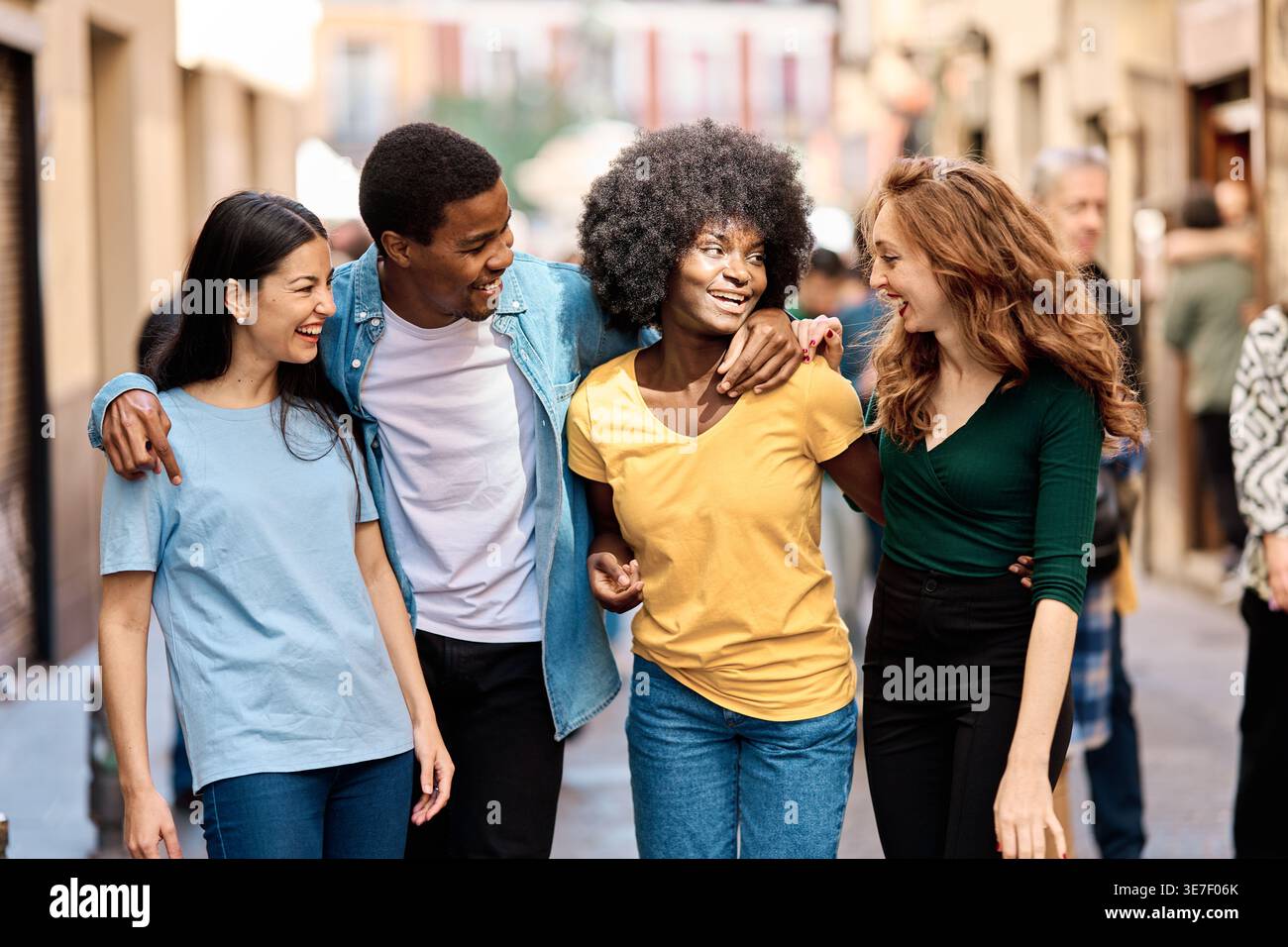 Cheerful Hispanic man having fun walking with Black and caucasian female friends on street during daytime Stock Photo