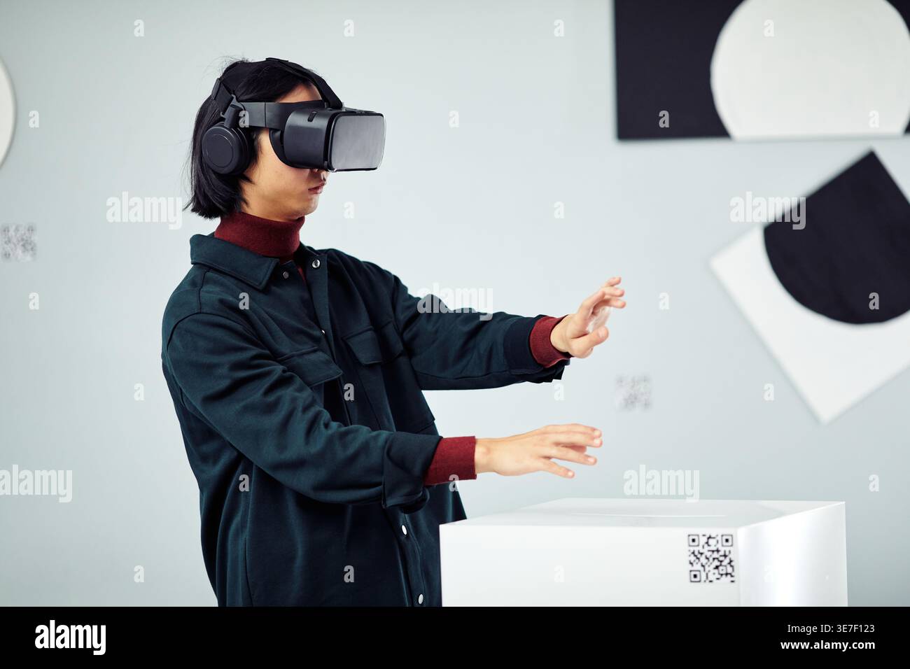 Asian man wearing VR headset experiencing virtual reality while standing in art gallery Stock Photo