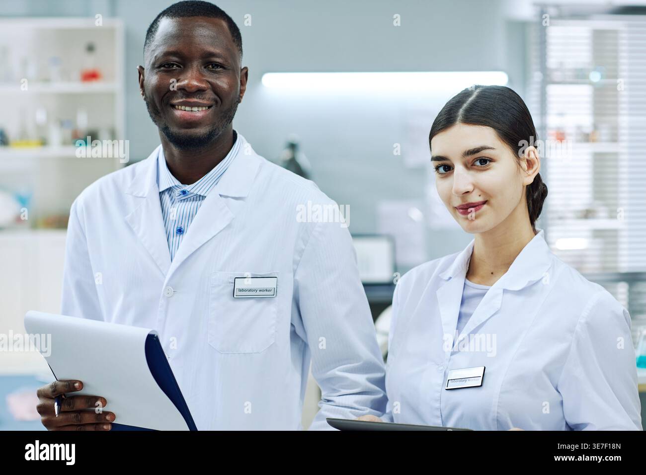 Smiling Black and mixed-race scientists wearing lab coat holding clipboards while standing together in laboratory Stock Photo