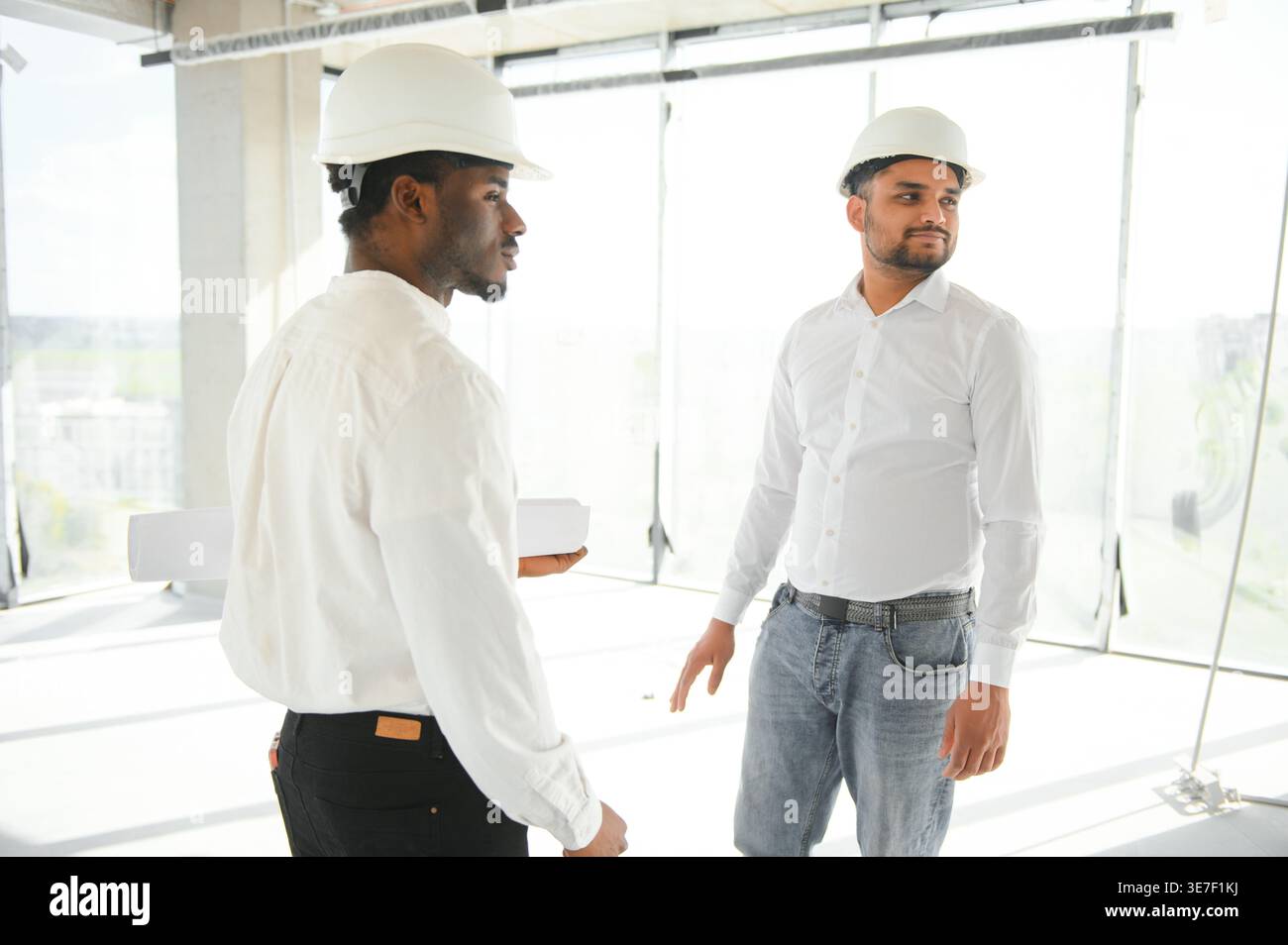 Diverse group of male engineers wearing hard hats walking together and doing inspection on construction site Stock Photo