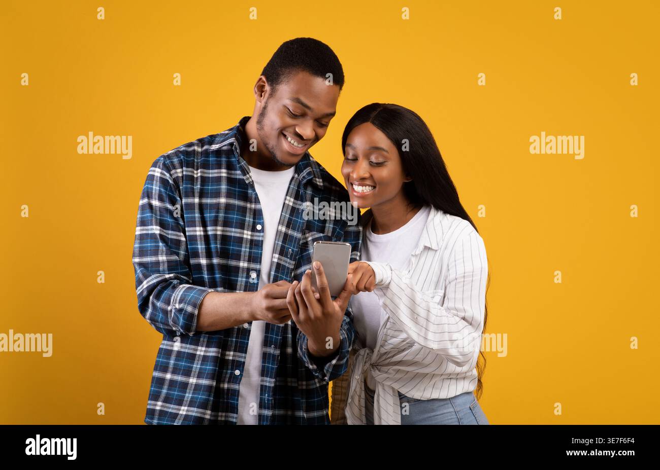 Black couple using smartphone together while standing against yellow background in studio Stock Photo