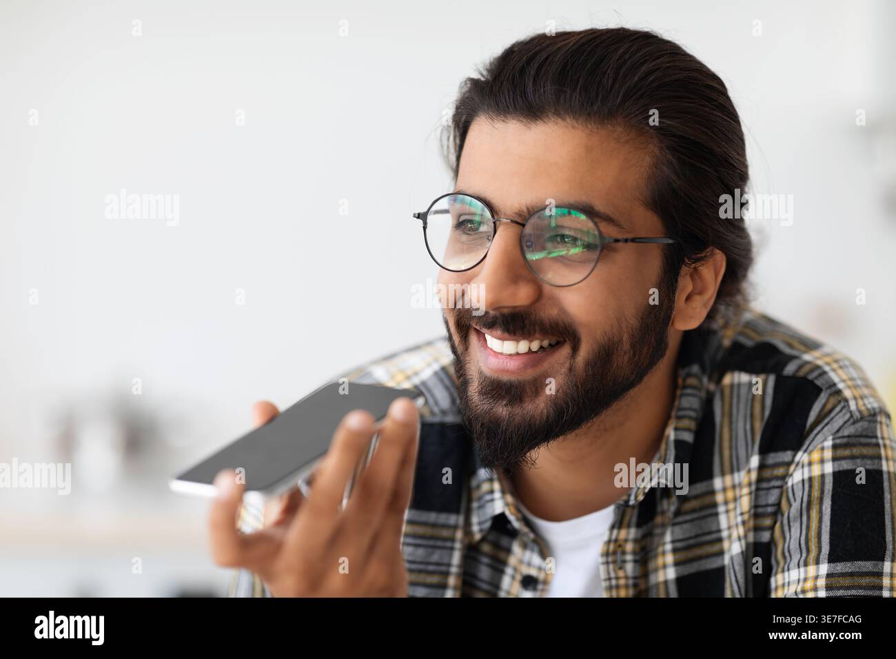 Arab man wearing eyeglasses having phone call looking away while standing at home Stock Photo