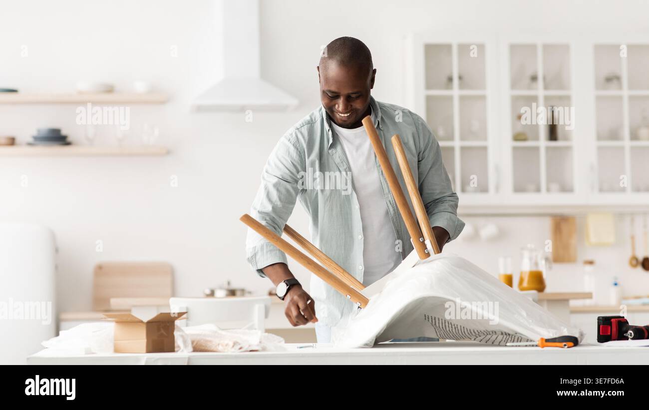 Black man assembling chair standing in kitchen at home Stock Photo