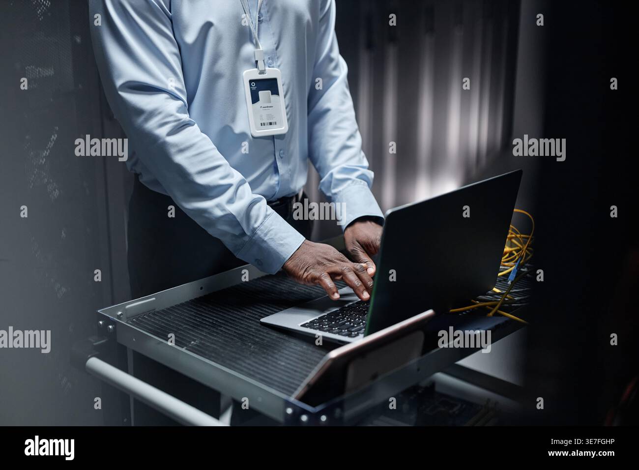Black male network engineer using laptop and setting up servers while standing in data center Stock Photo