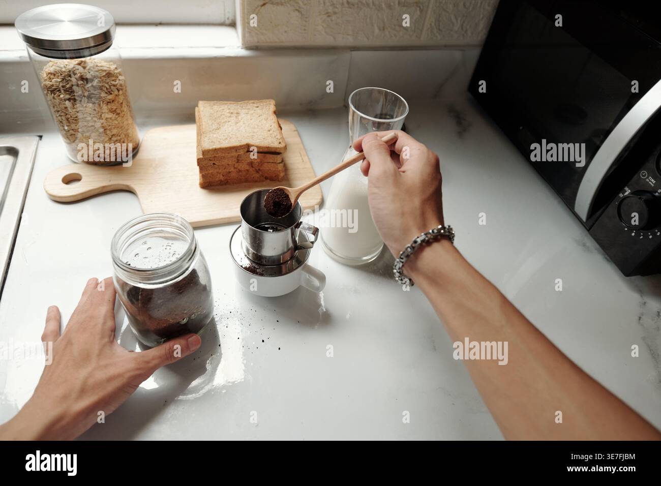 Cropped image of Asian male putting ground coffee into brewer while making coffee in kitchen at home Stock Photo