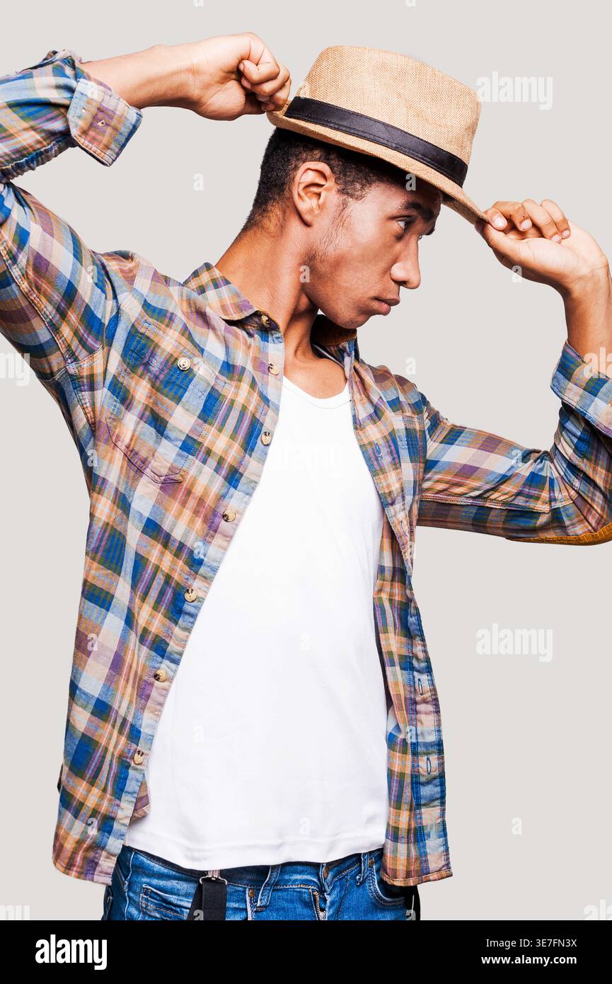 Black man looking sideways tipping straw hat while standing against light gray background Stock Photo