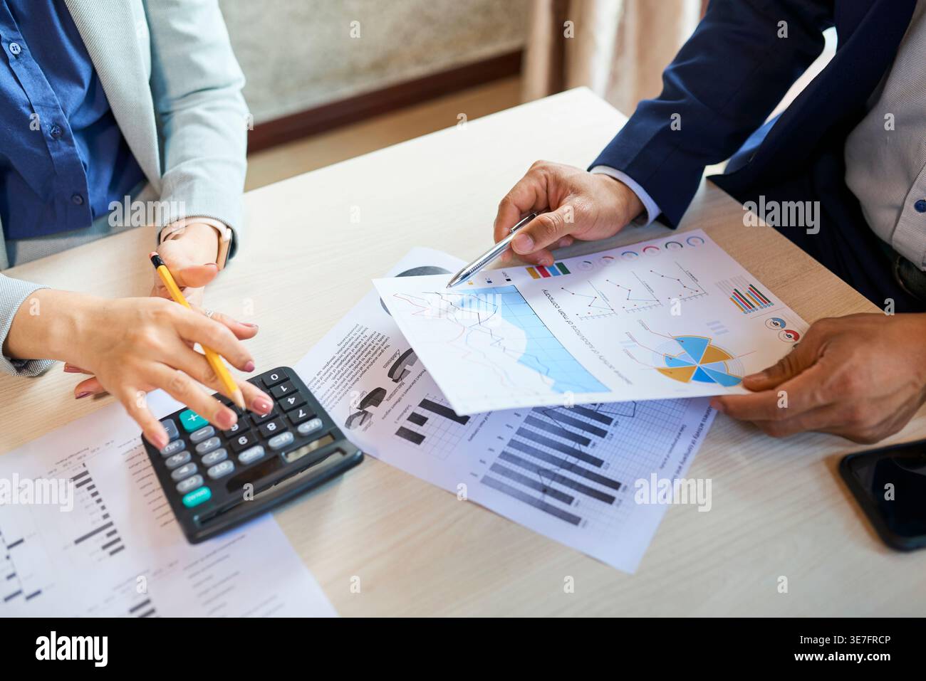 Asian managers using calculator analyzing various reports sitting at table in office during daytime Stock Photo