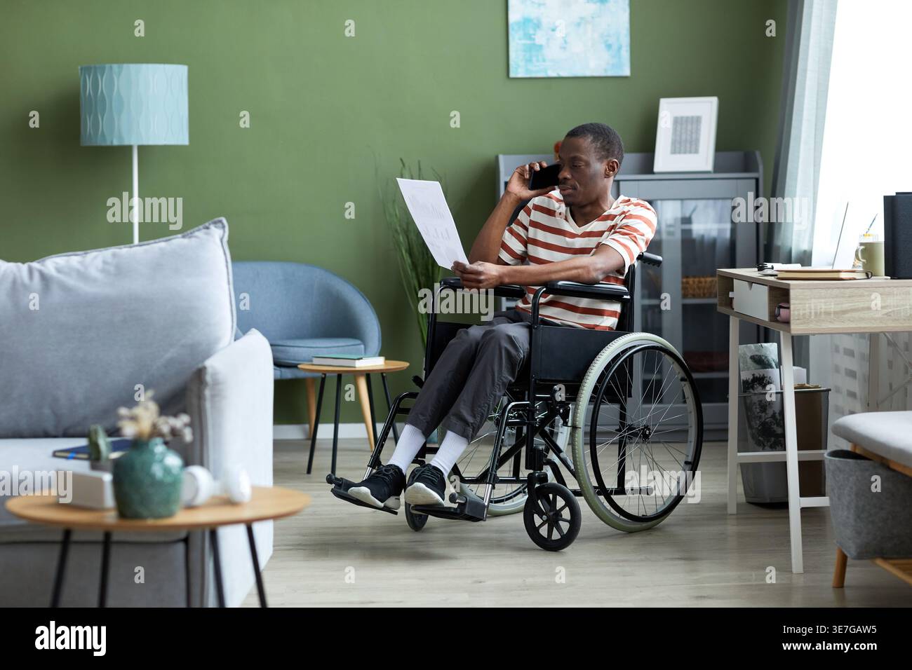 Disabled Black man in wheelchair having phone call and reviewing document report working from home Stock Photo