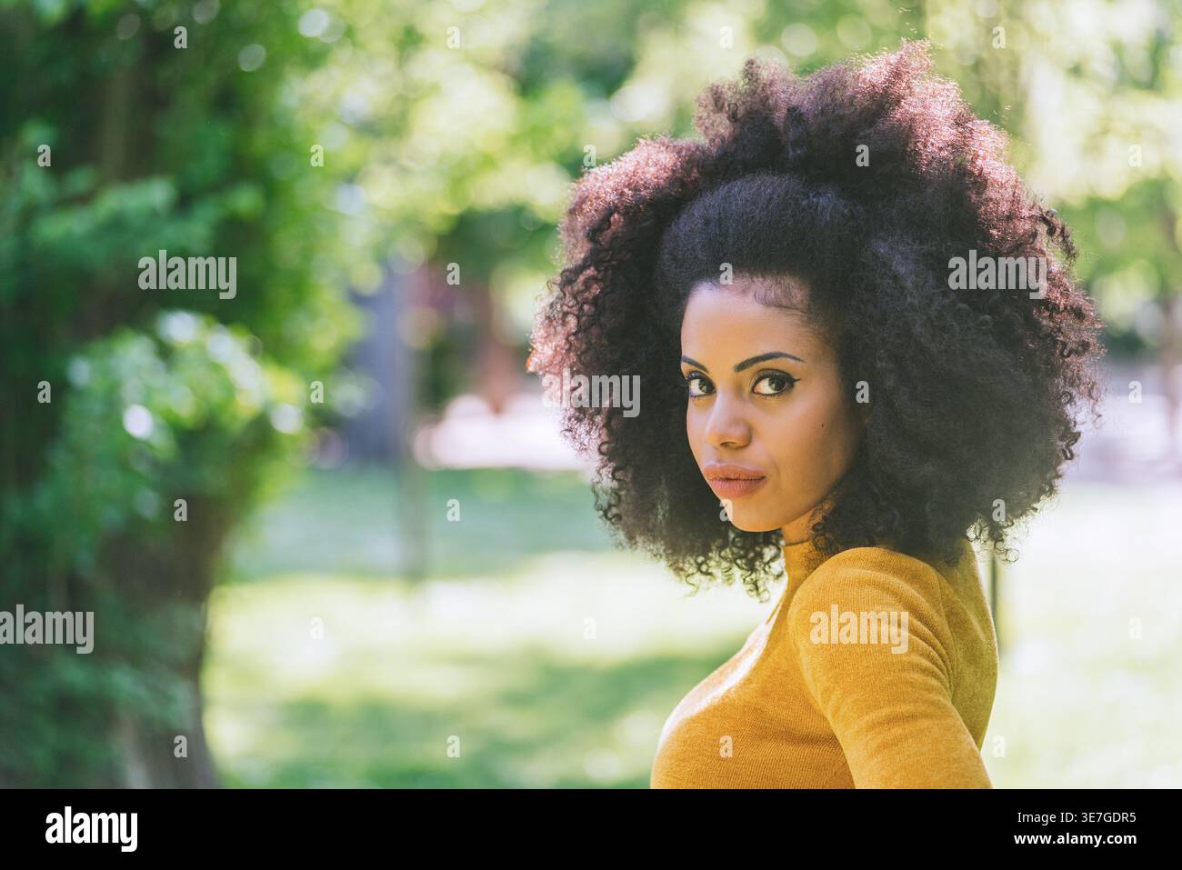 Hispanic female with curly hair looking sideways standing in park during daytime Stock Photo