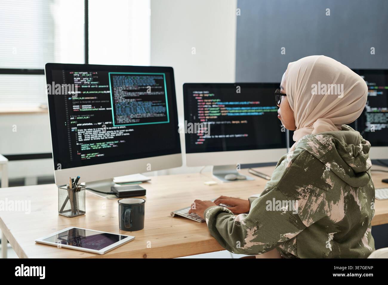 Mixed-race Muslim female software developer decoding data working on laptop sitting at table in office Stock Photo
