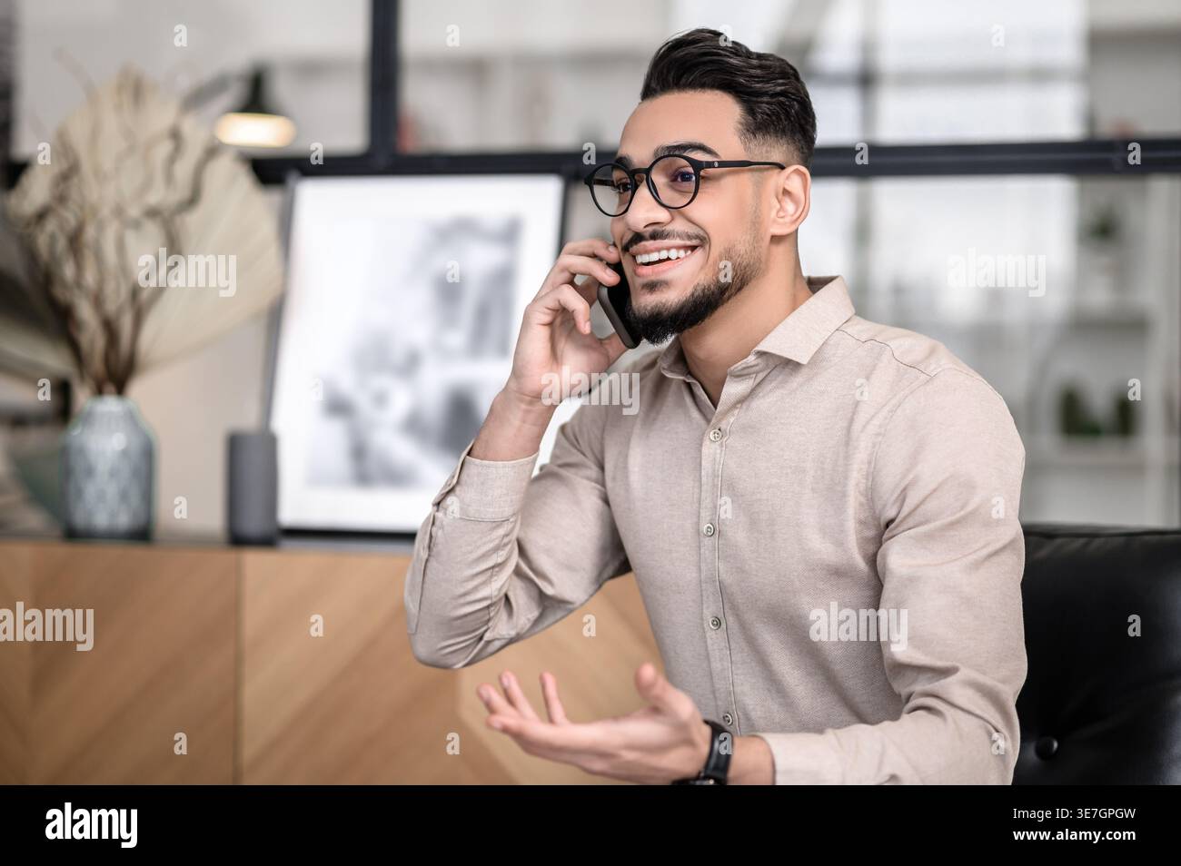 Smiling Arab man wearing eyeglasses having phone conversation standing at home Stock Photo