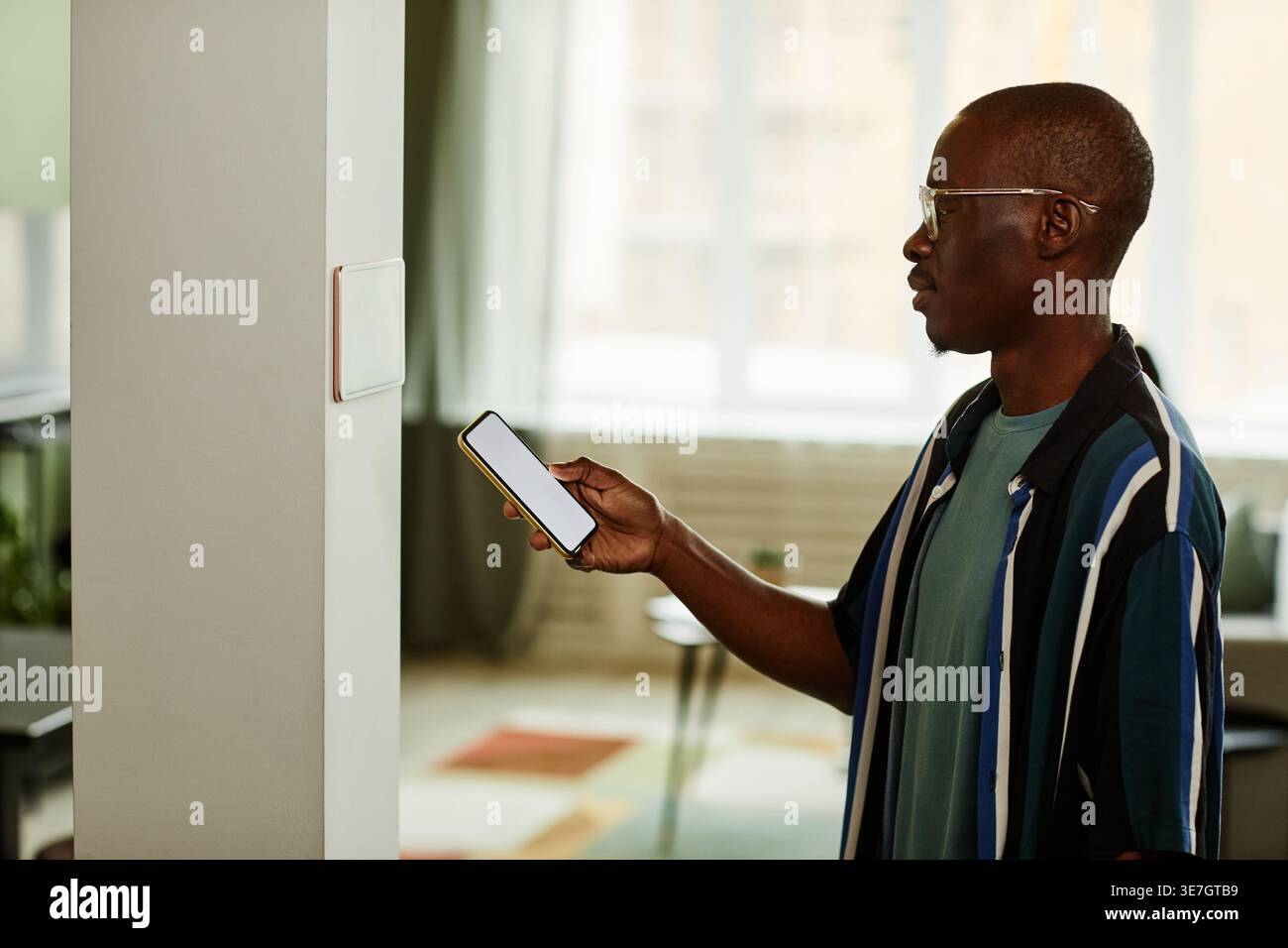 Black man using smartphone while connecting to smart home system standing indoors Stock Photo