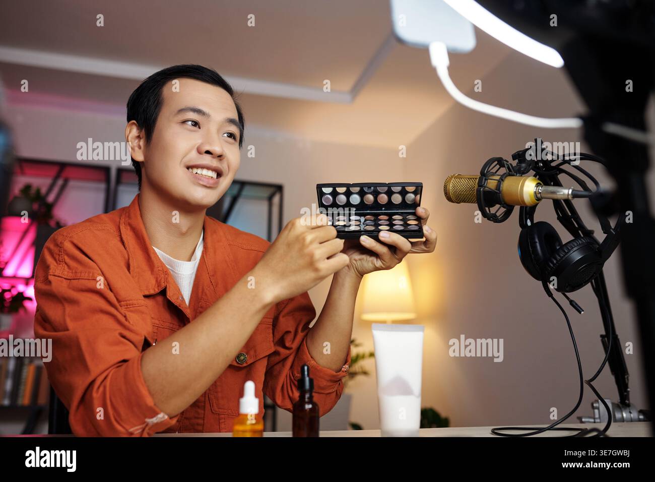 Asian man making video for blog demonstrating new eyeshadow palette at home Stock Photo