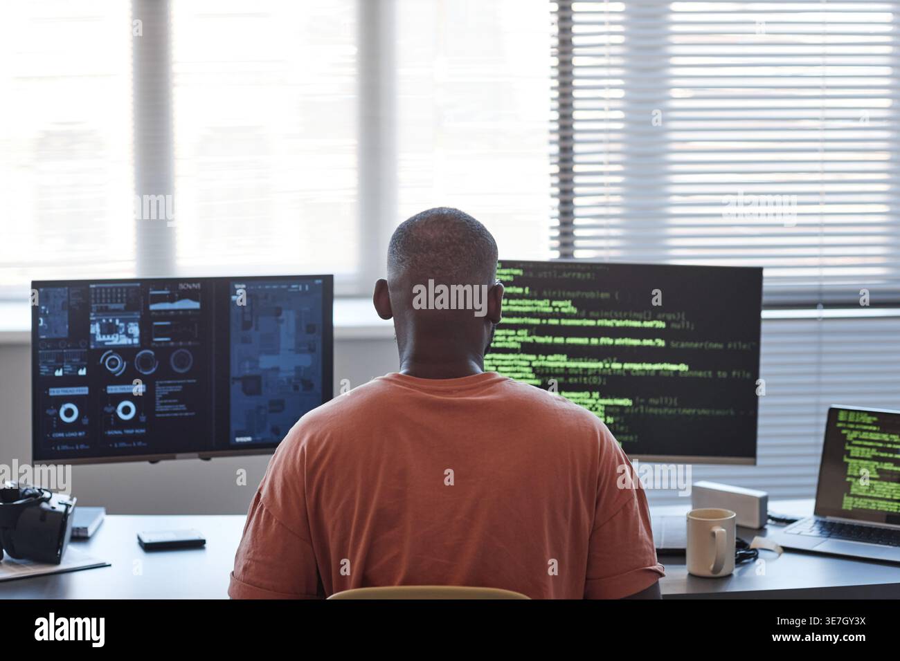 Back view of Black male programmer examining codes on computer while sitting at table in office Stock Photo