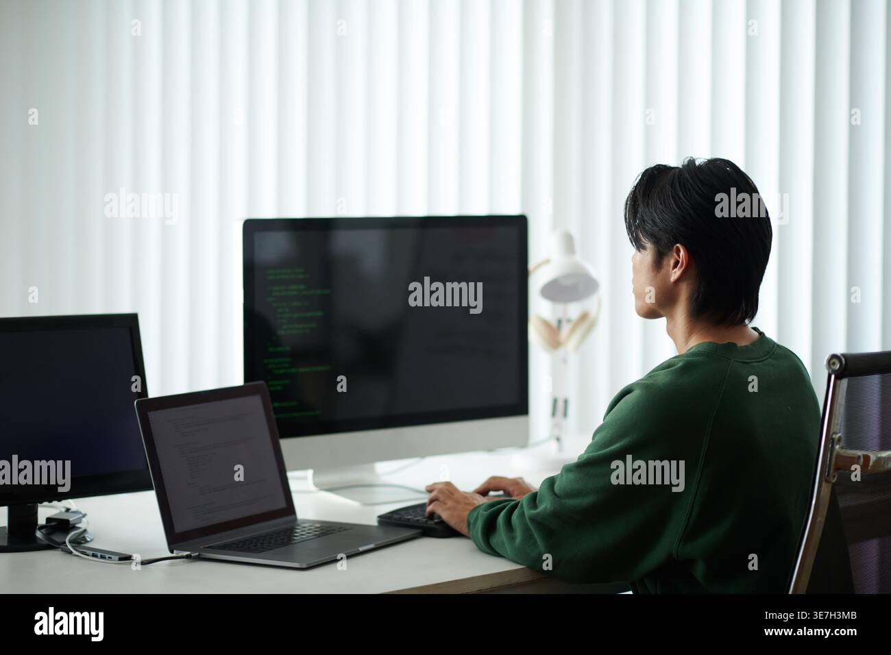 Asian male programmer typing codes on computer while sitting at table with laptop in office Stock Photo