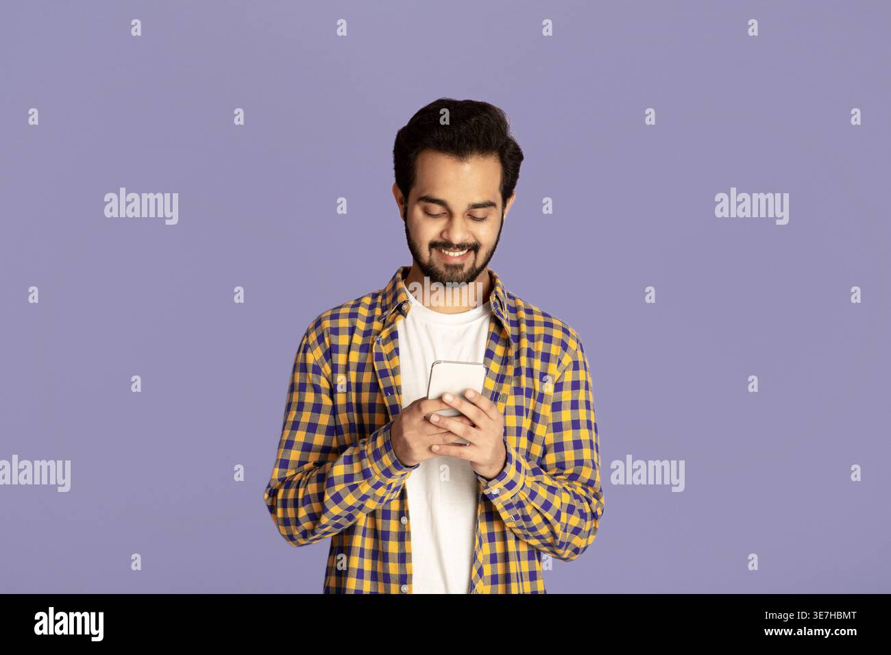 Indian man using smartphone standing against purple background in studio Stock Photo