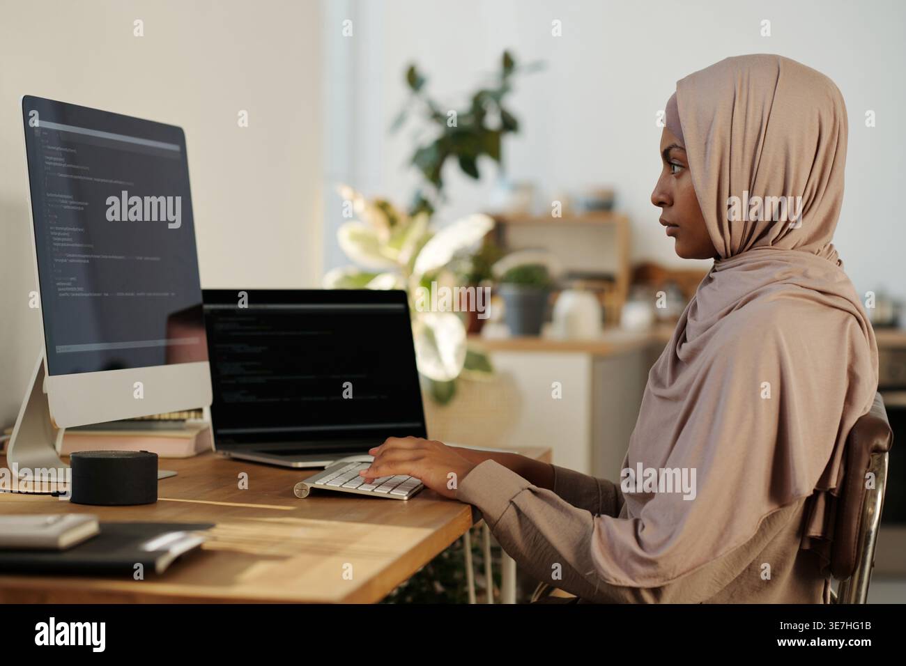 Black female programmer in hijab working codes on computer while sitting at table at home office Stock Photo