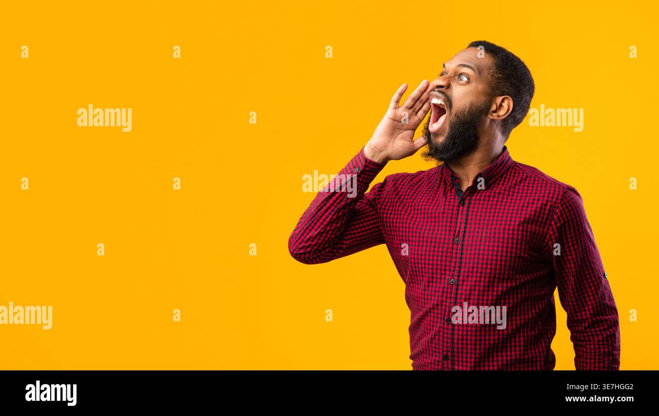Black man looking away and shouting while standing against yellow background in studio Stock Photo